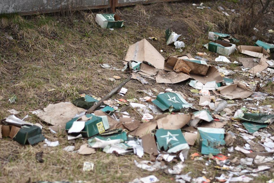 A pile of discarded cardboard boxes, some flattened and others partially intact, rests against a textured concrete brick wall outdoors. The boxes vary in size, with some displaying visible printing an